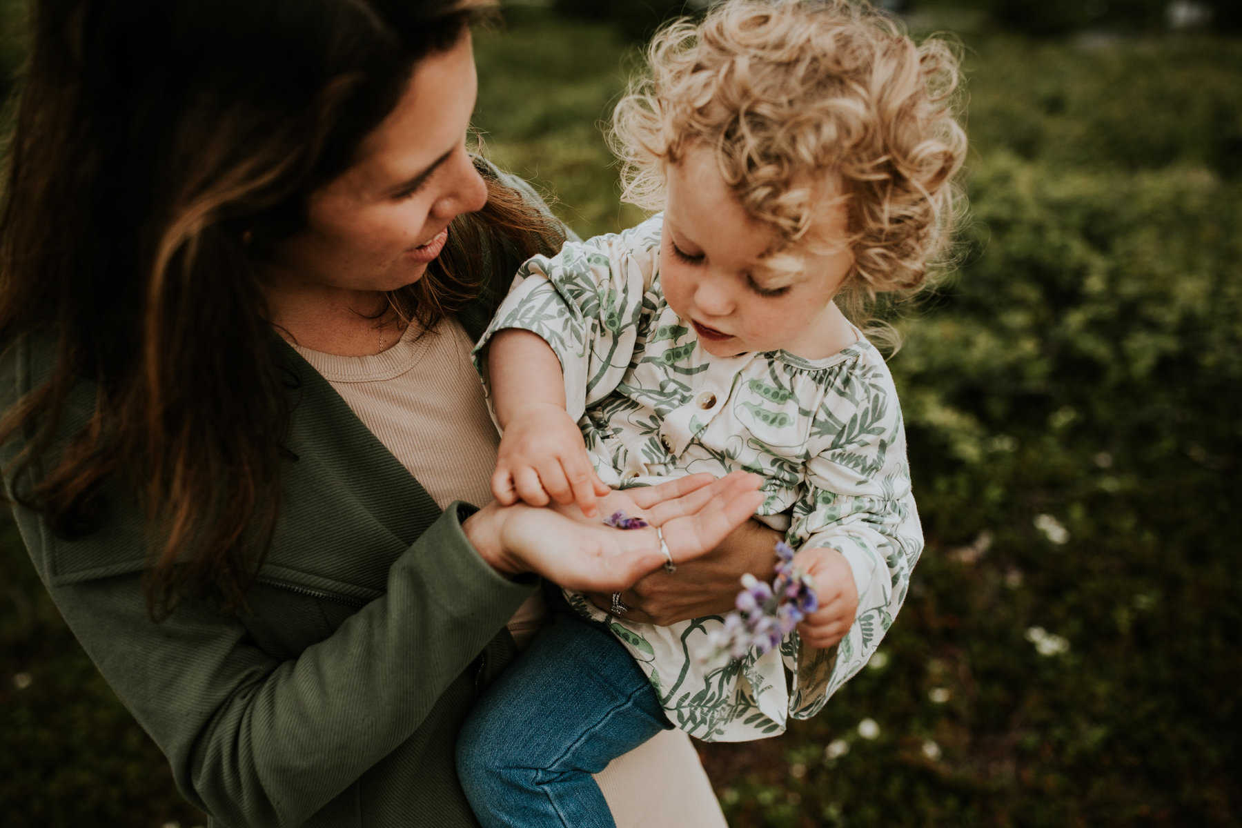 Mother holding baby daughter close, exploring nature, showing her a flower