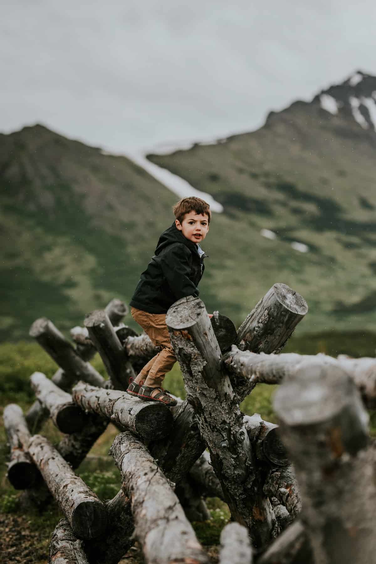 boy climbing a log fence with mountains in background