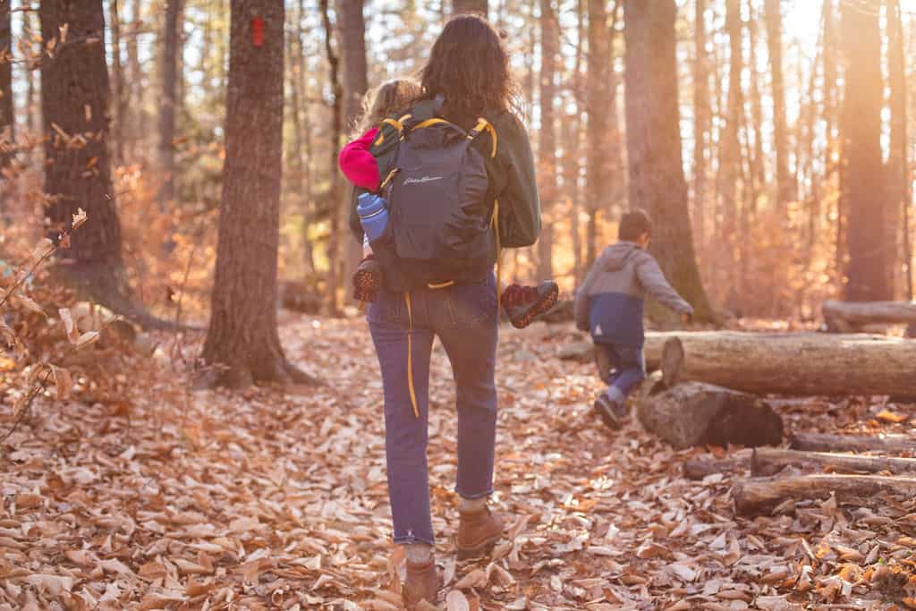 mother holding child hiking through woods with son running ahead