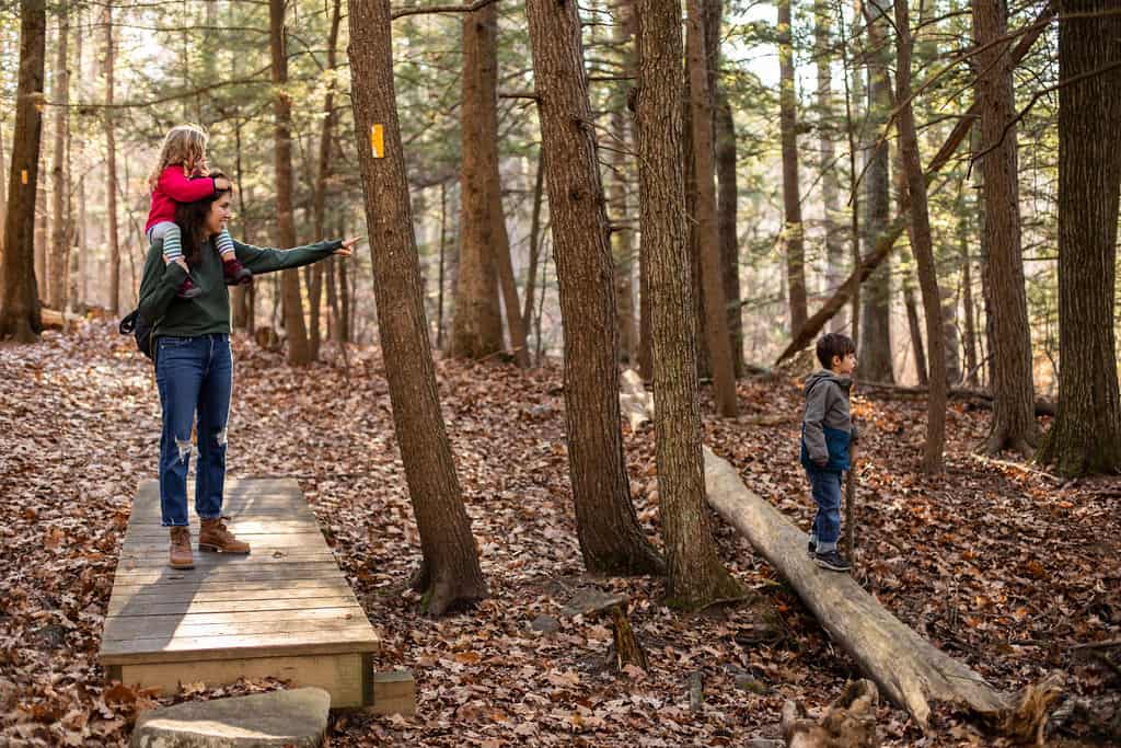 mother hiking with two kids carrying daughter on shoulders pointing