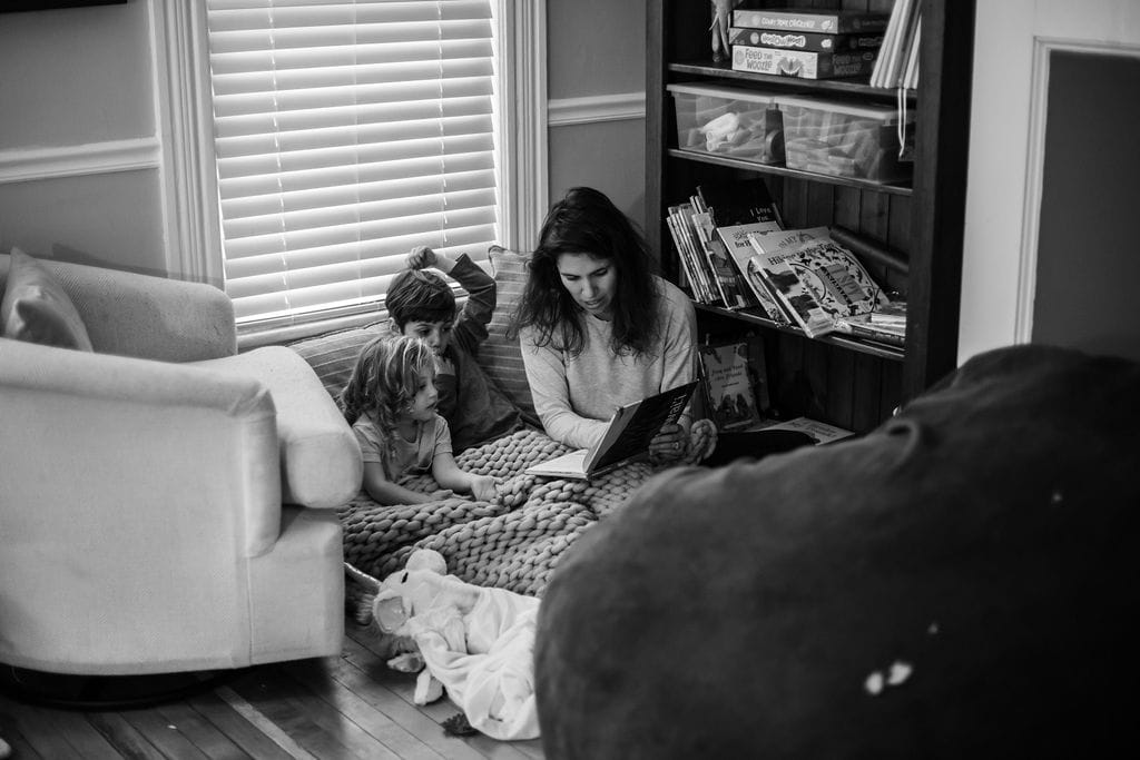 mother and two children slowing down and reading books together on floor