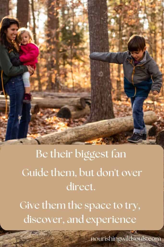mother holding daughter watching son balance on logs in woods. family working together