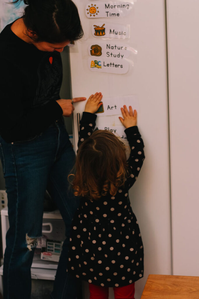 mom pointing to toddler schedule with little girl putting card on schedule