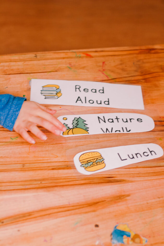 three cards from a toddler schedule with toddler hand pointing at one