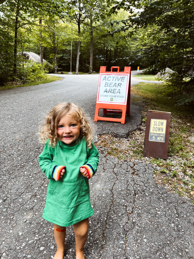 little girl camping with family standing in front of bear sign pretending to be scare. camping gifts
