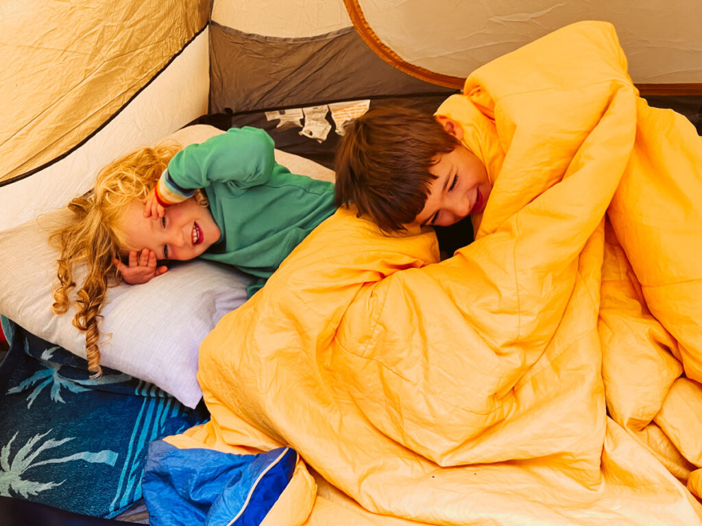 two kids playing in a tent and in their cozy camp blankets and sleeping bags