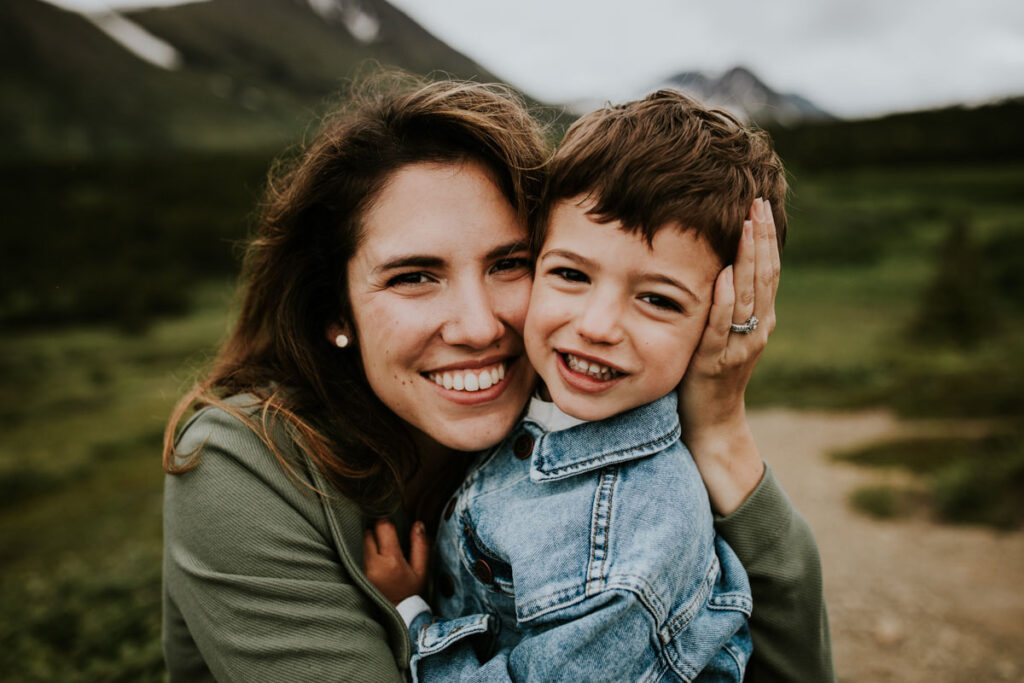 Mother holding son and both smiling while during family portraits outside