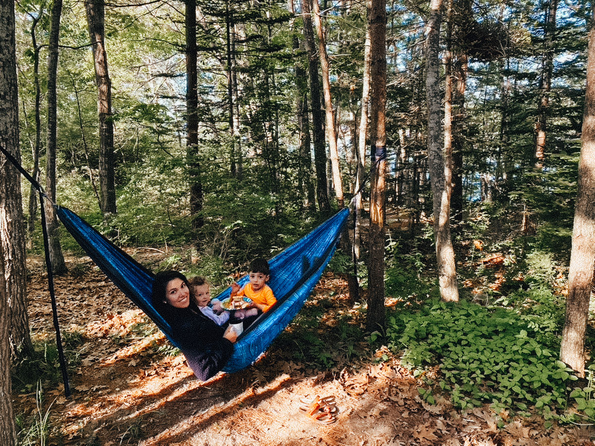 add a hammock to your camping packing list for families, a family enjoying a hammock while camping